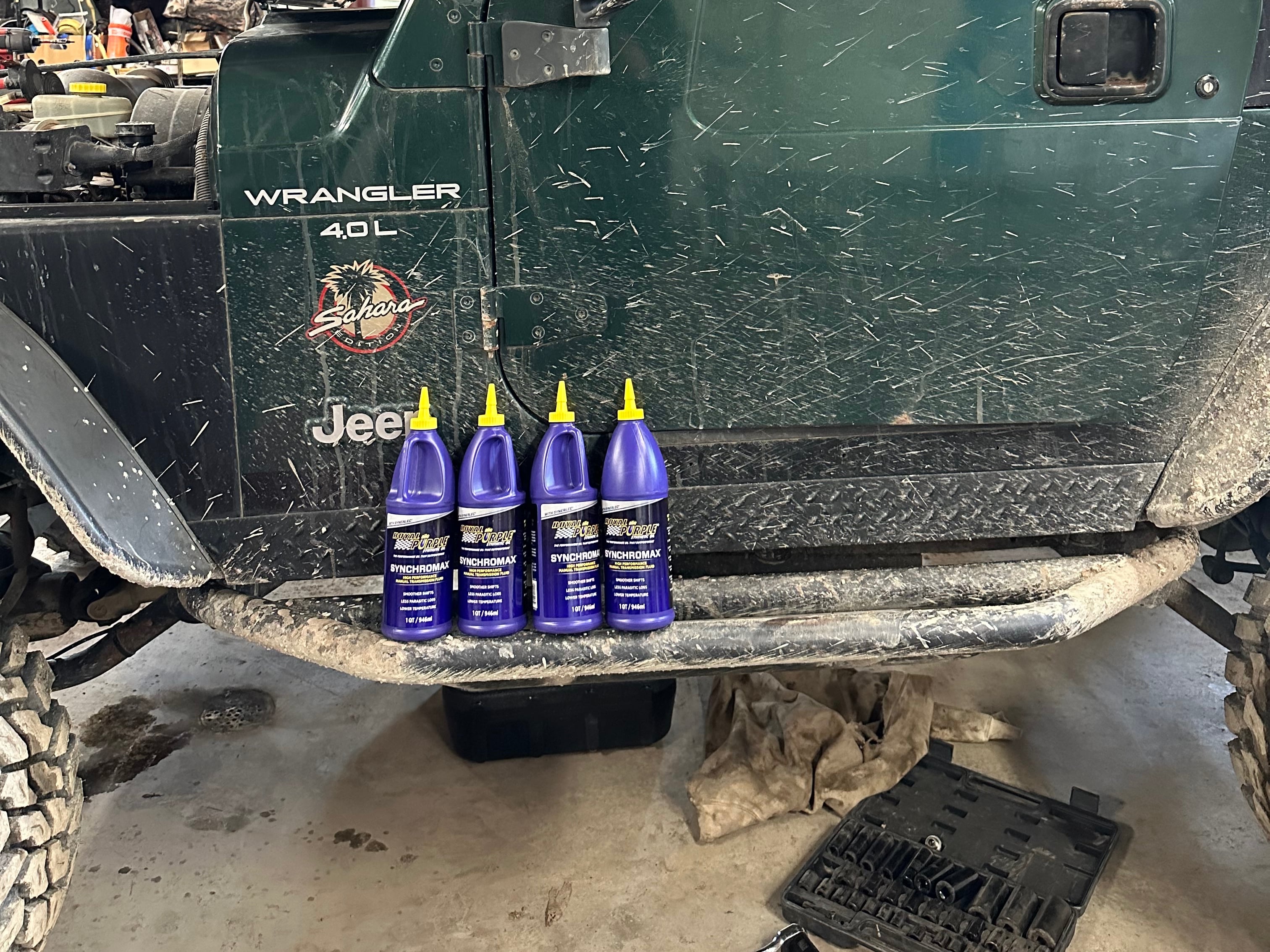 Royal Purple Synchromax manual transmission fluid lined up beside a Jeep Wrangler TJ, illustrating the fluid used for manual transmission service.